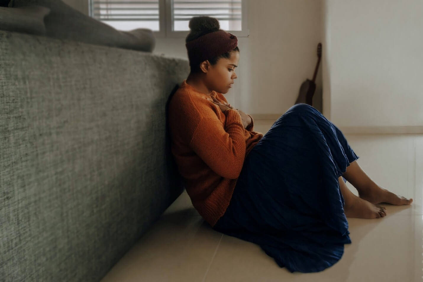 A young Black woman sits on the floor looking depressed.