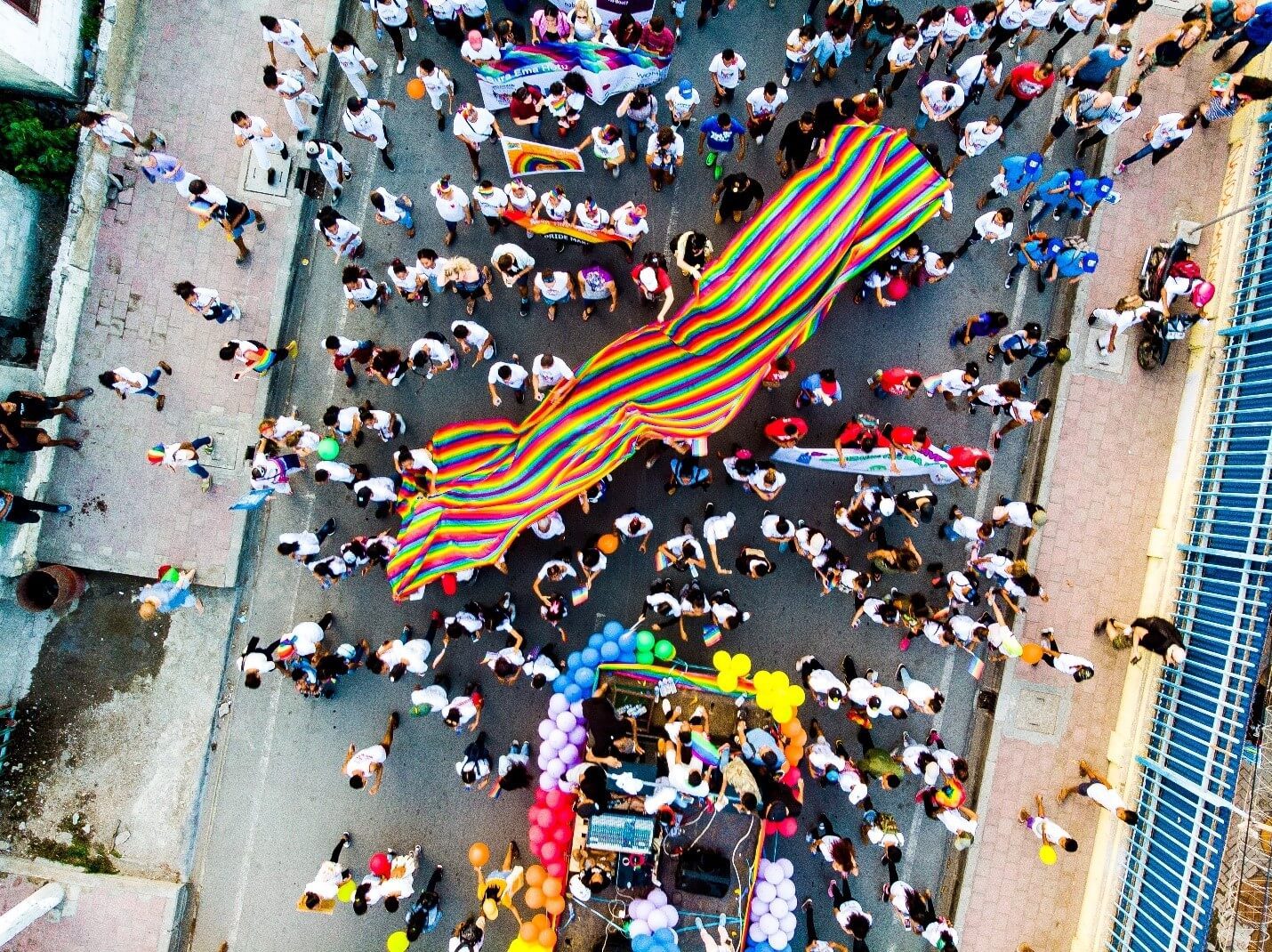A view from above of a large crowd holding a Pride flag in the street