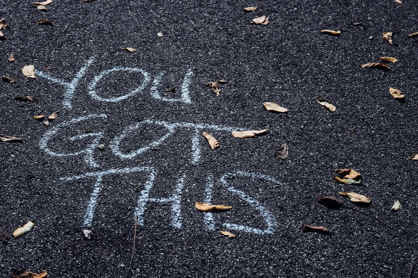 An asphalt surface with 'you Got This' written in white chalk.