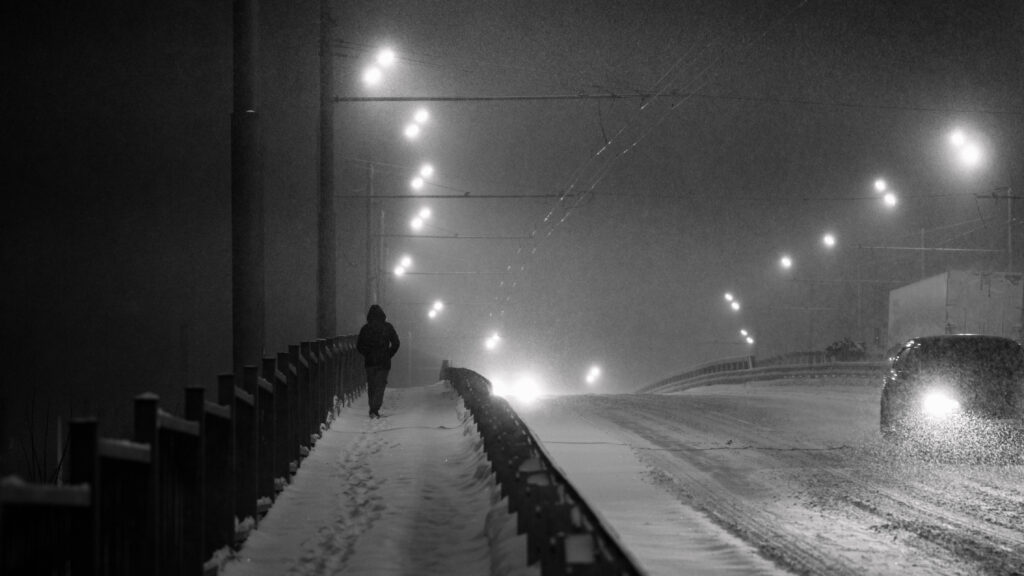silhouette of a man walking through a snow-covered city in a heavy snowstorm, black and white photo